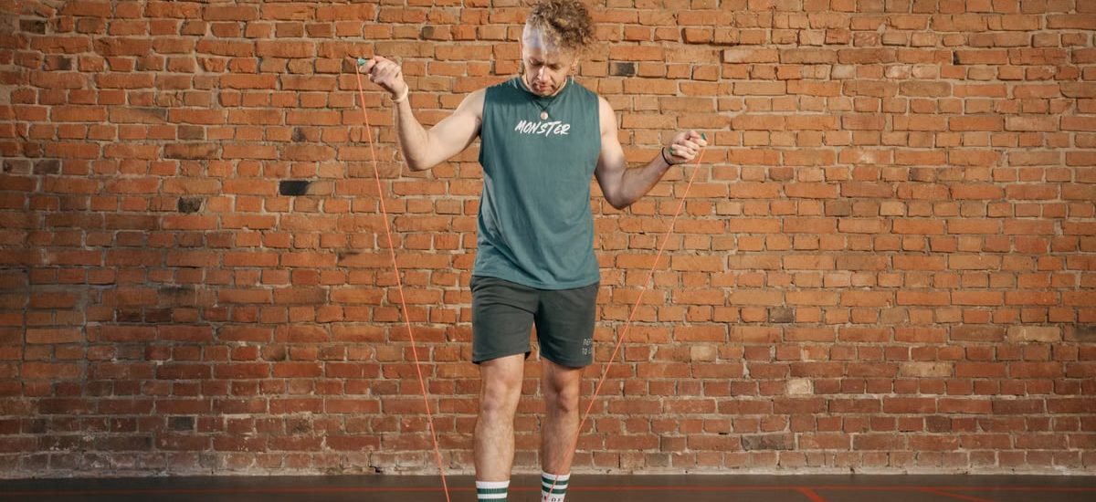 Caucasian man engaging in a jump rope workout in an indoor setting with a brick wall background.