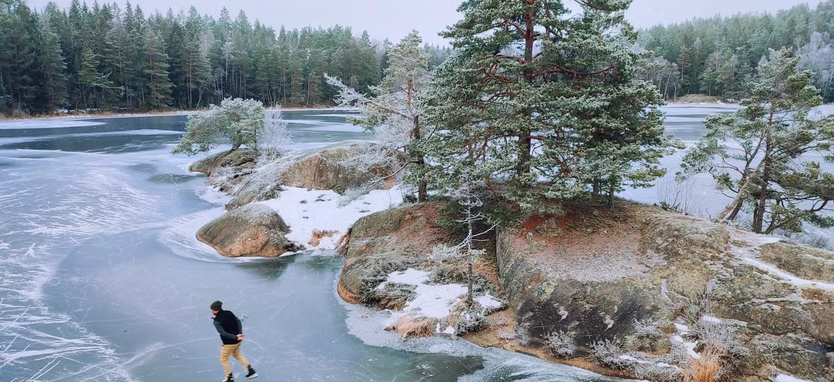 A person ice skating on a frozen lake surrounded by snowy trees, creating a serene winter scene.